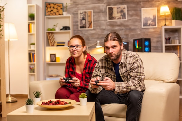 Gamers couple playing video games on the TV with wireless controllers in hands.