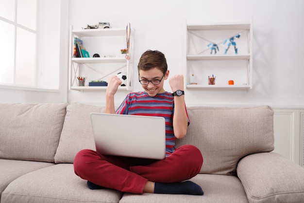 Gaming online. Excited teenage boy playing online game on laptop, enjoying win while sitting on sofa in living room at home