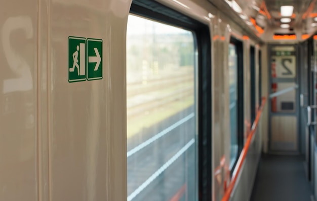 Gangpad van trein naast coupécabines, wazig landschap achter raam, foto met ondiepe scherptediepte, focus op groen nooduitgangbord aan muur