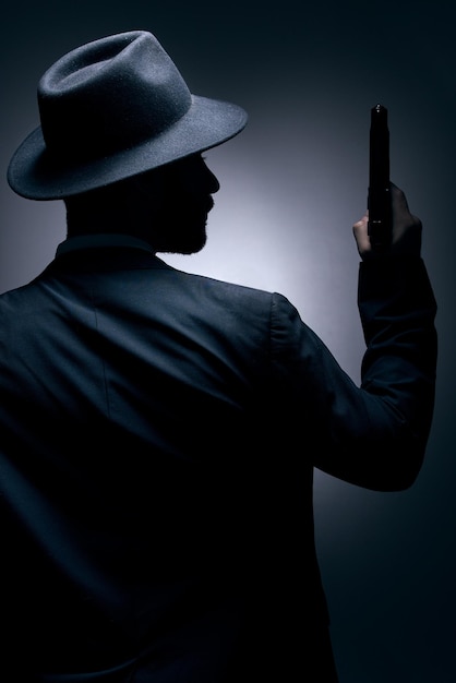 Фото Гангстерский силуэт или держащий пистолет на студийном фоне в секретном шпионском изолированном мафиозном лидерстве или криминальной безопасности