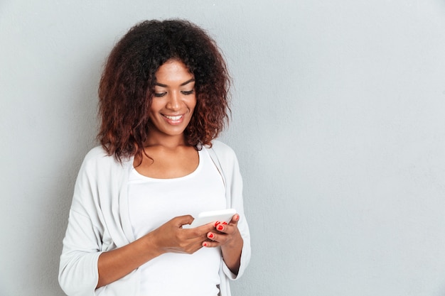 Gappy smiling african woman typing message on mobile phone