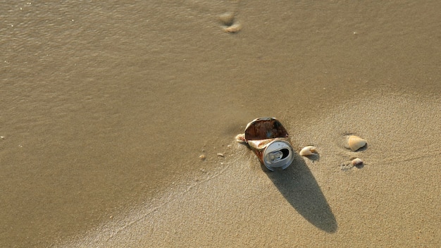 Garbage, aluminum can, on the beach with shells on sand on summer.