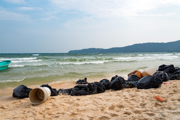 해변의 쓰레기 환경 오염 아시아 섬의 모래에 있는 검은색 쓰레기 봉투 해변의 자연 쓰레기 수거 쓰레기 수거 청소