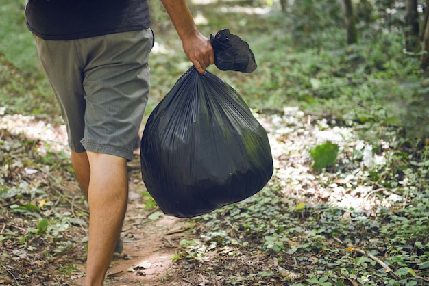 ゴミ収集エコロジー、公園の清掃、黒いプラスチック製のゴミ袋を持っている人間の手