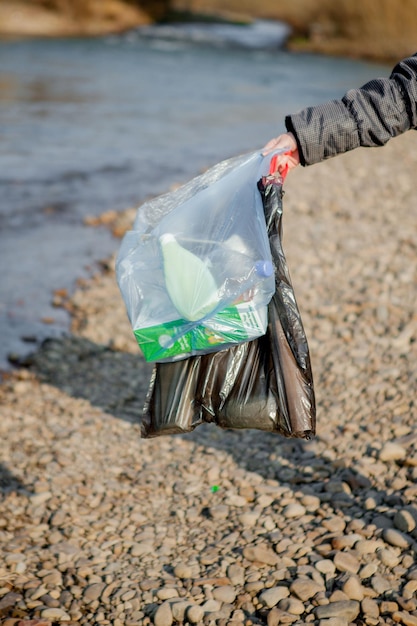 사진 봄철 강가에서 환경을 청소하는 자연의 쓰레기 일회용 라텍스 파란색 장갑을 끼고 파란색 큰 비닐 봉지에 넣은 여성