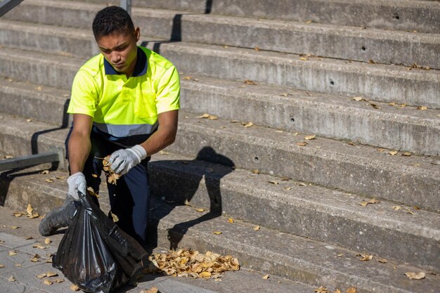 Garbage man picking up leaves in a rubbish bag, with gloves,
stairs at the background