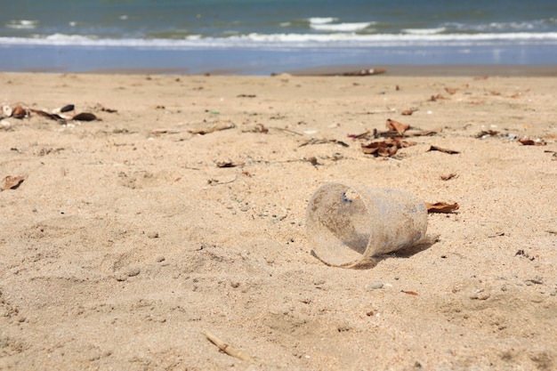 写真 夏の朝の砂の上の貝殻とビーチのゴミプラスチックガラス環境と自然