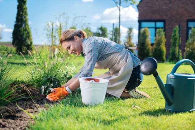 Garden bed. Good-looking woman feeling joyful and happy while leaning on her garden bed planting new little flowers