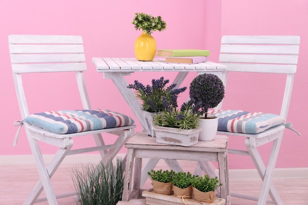 Garden chairs and table with flowers on wooden stand on pink