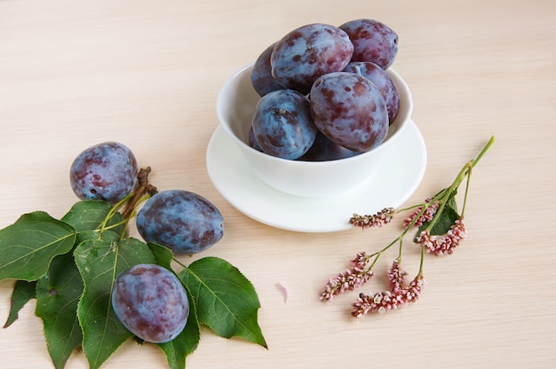 Garden plums in a white cup on a wooden table