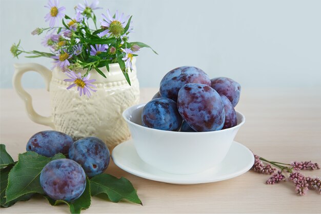 Garden plums and wildflowers on a light wooden surface