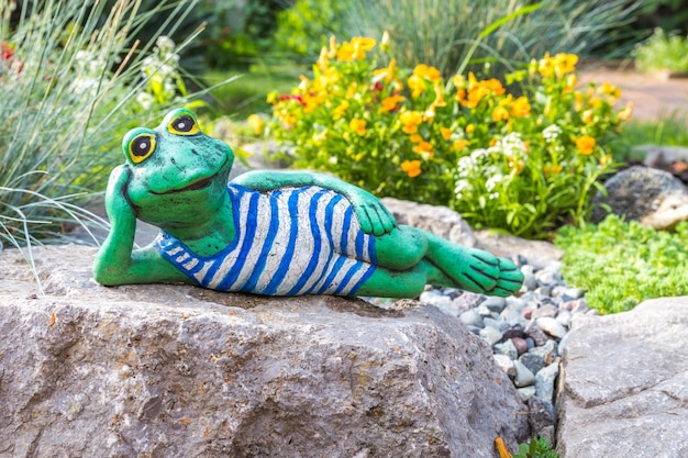 A garden sculpture of a frog lying on the floor reading a book