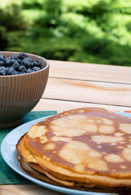 in the garden on the table there is a cup with fresh blueberries and a plate of blits