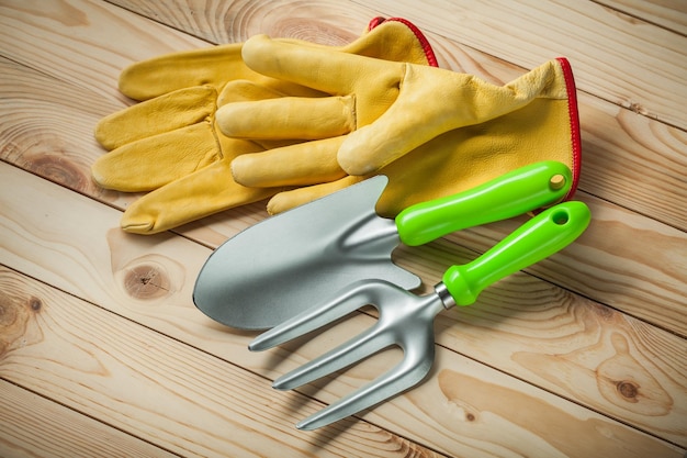 Garden tools. hand spade and fork with yellow leather gloves on wooden background