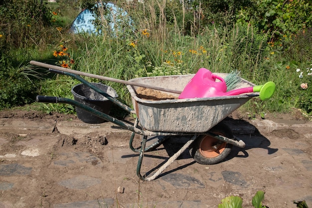 На дорожке в саду стоит садовая тачка, наполненная песком и сухой цементной смесью.