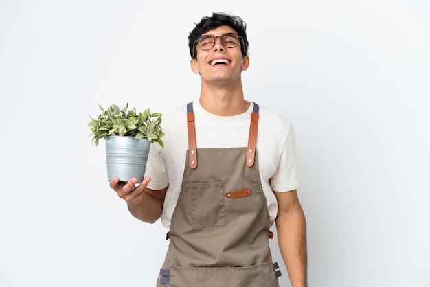 Gardener Argentinian man holding a plant isolated on white background laughing