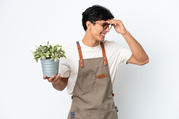 Gardener Argentinian man holding a plant isolated on white background laughing