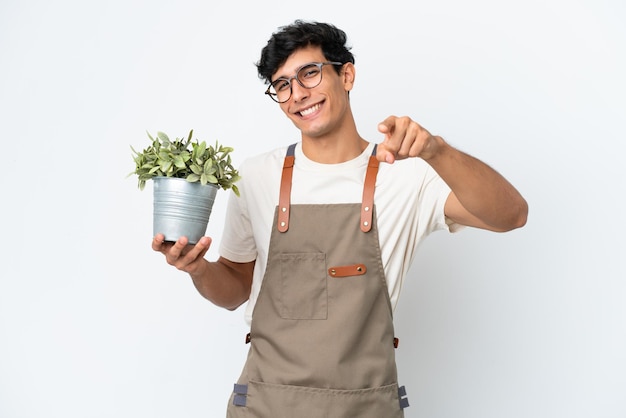 Аргентинский садовник держит растение на белом фоне, указывая вперед со счастливым выражением лица