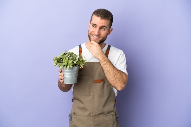Gardener caucasian man holding a plant isolated on yellow background looking to the side and smiling