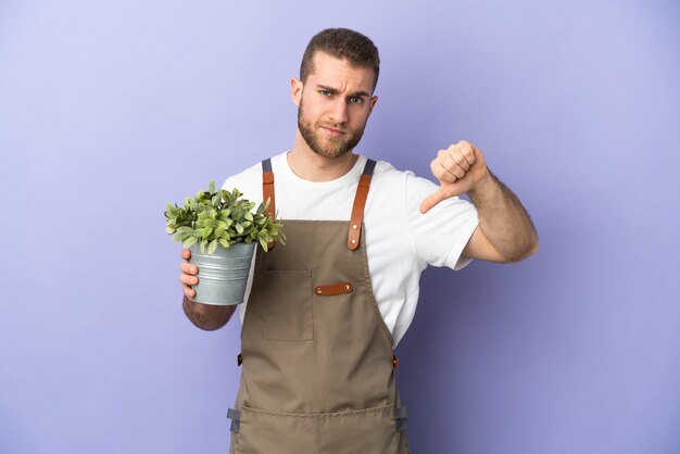 Gardener caucasian man holding a plant isolated on yellow showing thumb down with negative expression