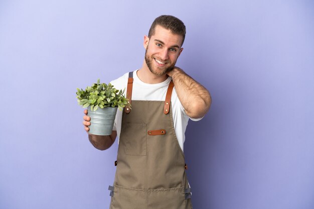 Gardener caucasian man holding a plant isolated on yellow wall laughing