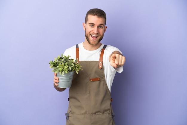 Gardener caucasian man holding a plant isolated on yellow wall surprised and pointing front