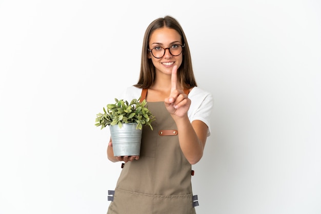 孤立した白い背景の上に植物を保持し、指を見せて持ち上げる庭師の女の子