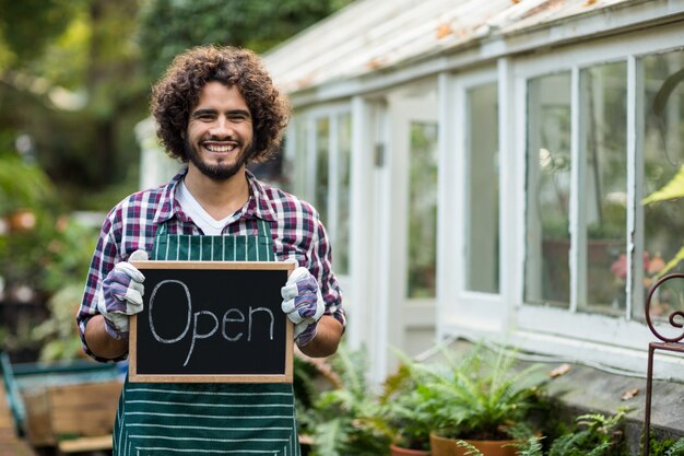 Gardener holding open sign placard outside greenhouse