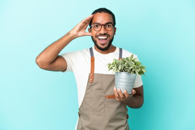Латиноамериканец-садовник держит растение на синем фоне с удивленным выражением лица