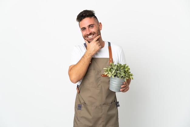 Gardener man holding a plant over isolated white background happy and smiling