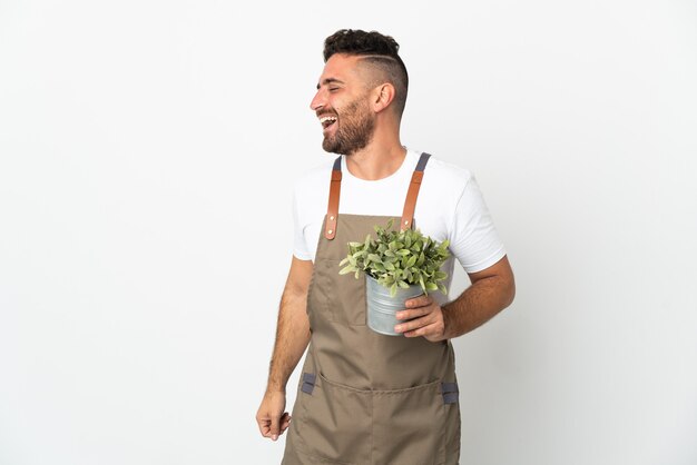 Gardener man holding a plant over isolated white background laughing in lateral position