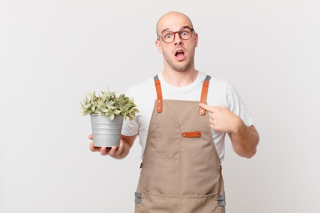 Gardener man looking shocked and surprised with mouth wide open, pointing to self