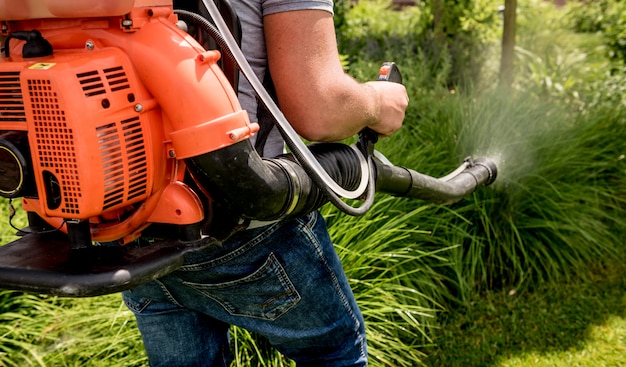 Gardener in protective mask and glasses spraying toxic pesticides trees