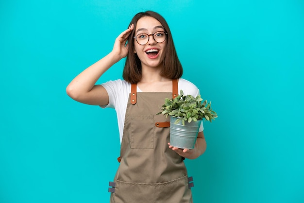 Gardener Ukrainian woman holding a plant isolated on blue background with surprise expression