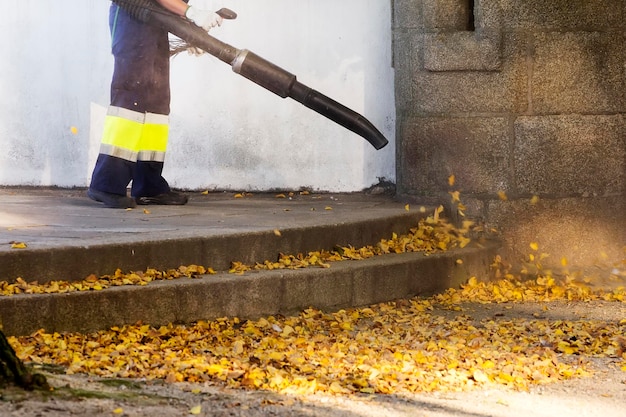 Foto giardiniere con zaino soffiante che lavora nel parco della città soffiando foglie