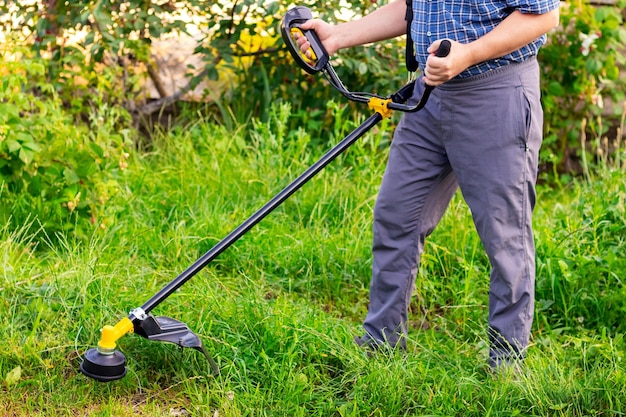 Il giardiniere con un decespugliatore falcia l'erba nel giardino