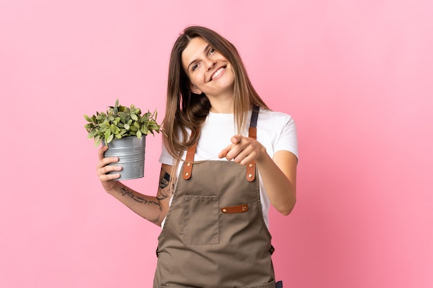 Gardener woman holding a plant isolated on pink pointing front with happy expression