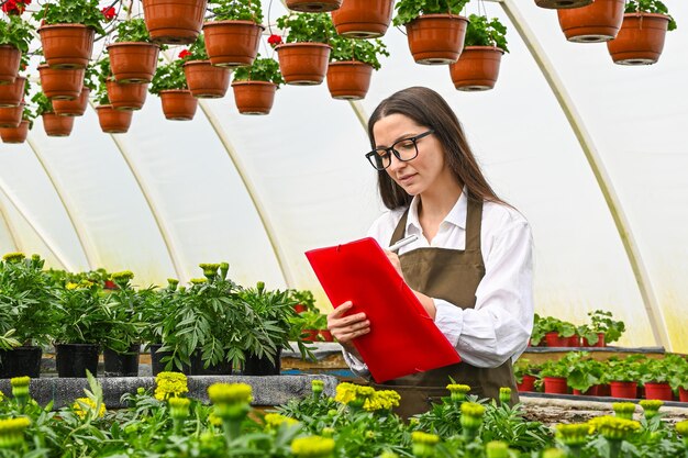 Donna giardiniere che lavora sui fiori in serra e prende appunti imprenditore che lavora sui fiori in serra