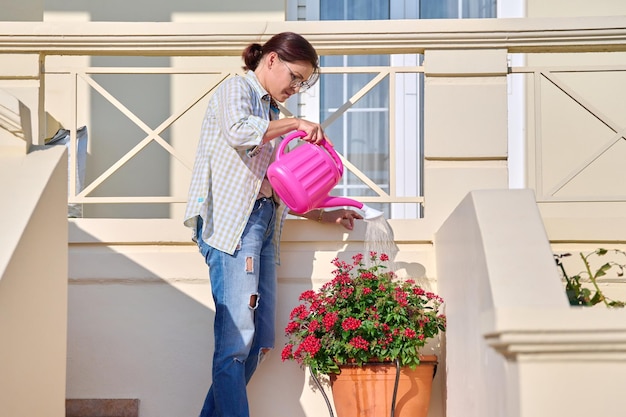 Gardening of balcony terrace porch woman waters flowering plants from watering can