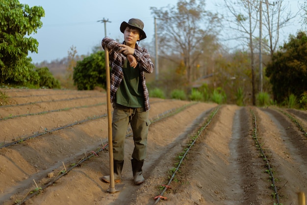 ガーデニングのコンセプトは、植物を育てる準備をする野菜畑を作るために土を掘る鍬を使用する男性農家です。