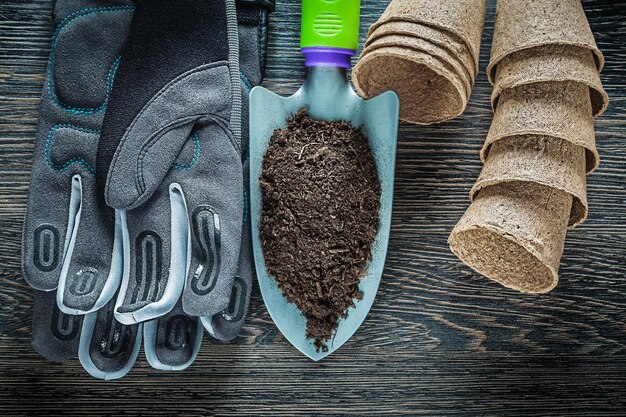 Gardening hand spade soil peat pots safety gloves on wooden board.