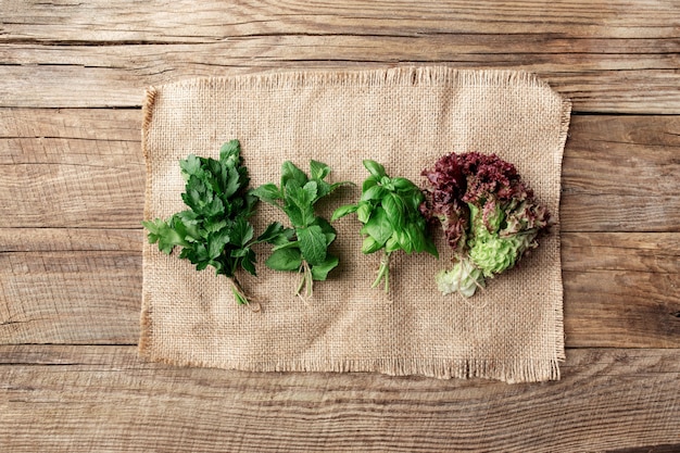 Gardening and healthy eating concept with different herbs and salad leaves, basil, mint, radicchio, parsley and celery on sackcloth on wooden background