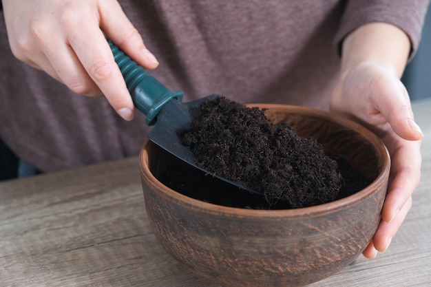 Gardening at home, womens hands pouring soil for plants into ceramic pot. Step by step, tutorial.