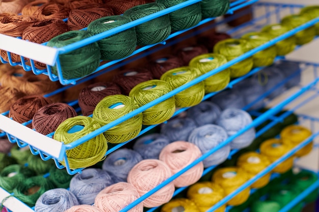 Garens of bolletjes wol op planken in de winkel voor breien en handwerken. Accessoires voor fournituren in stoffen winkelrekken. Veelkleurige foto, achtergrond.