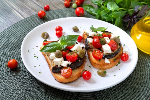 Garlic bruschetta with eggplant, feta, cherry tomatoes, capers. Useful vegetarian appetizer. Italian Cuisine.