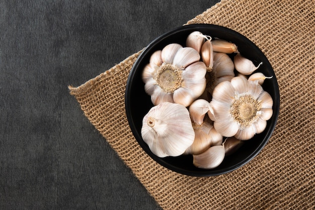 Garlic Cloves and Bulb in black bowl on jute and dark background.