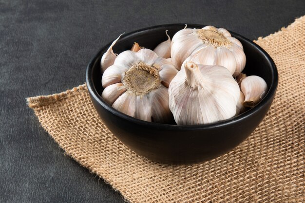 Spicchi d'aglio e lampadina in ciotola nera su iuta e sfondo scuro.