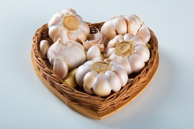 Garlic Cloves and Bulb in Heart Basket on White Background.