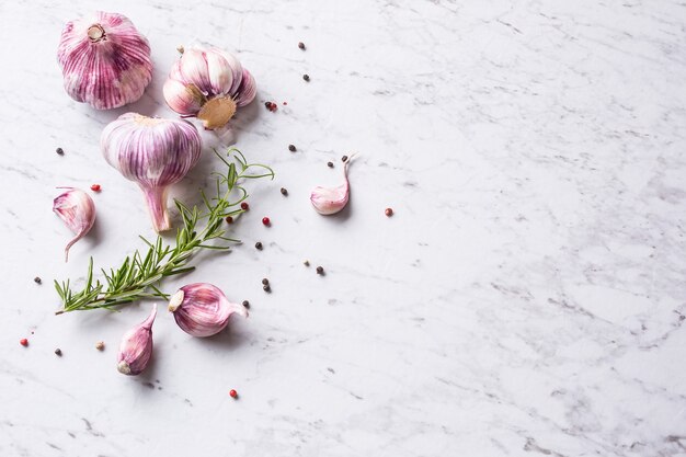 Garlic Cloves and Bulbs with rosemary salt and pepper on white marble board.