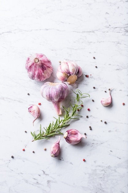 Garlic Cloves and Bulbs with rosemary salt and pepper on white marble board.